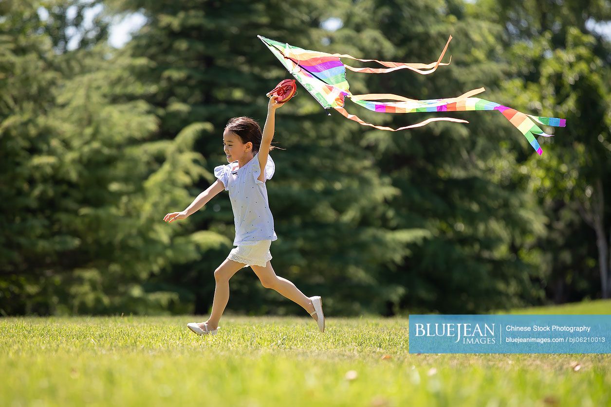 Happy little Chinese girl running with a kite on meadow