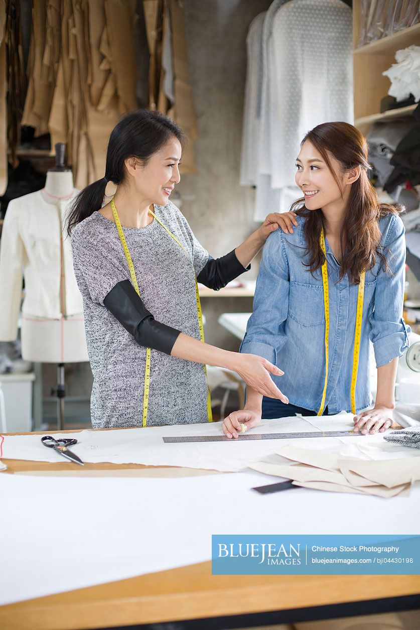 Two Chinese female fashion designers talking in studio