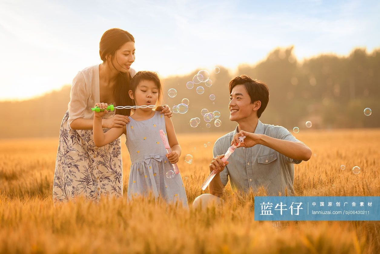 快乐的年轻家庭在麦田里吹泡泡