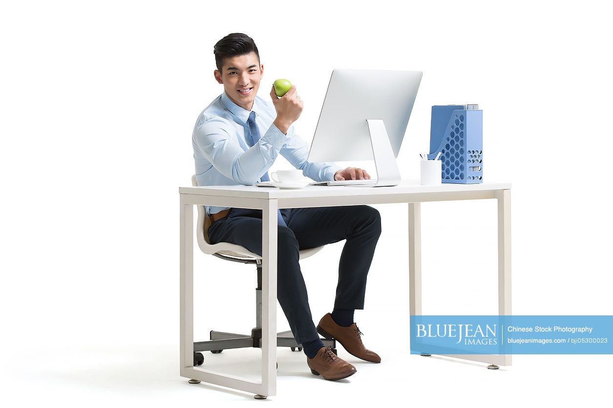 Young Chinese businessman working with computer in office holding apple