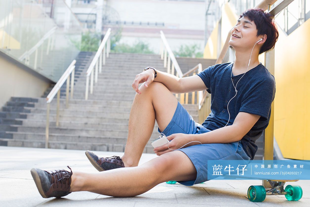 年轻男子坐在滑板上听音乐