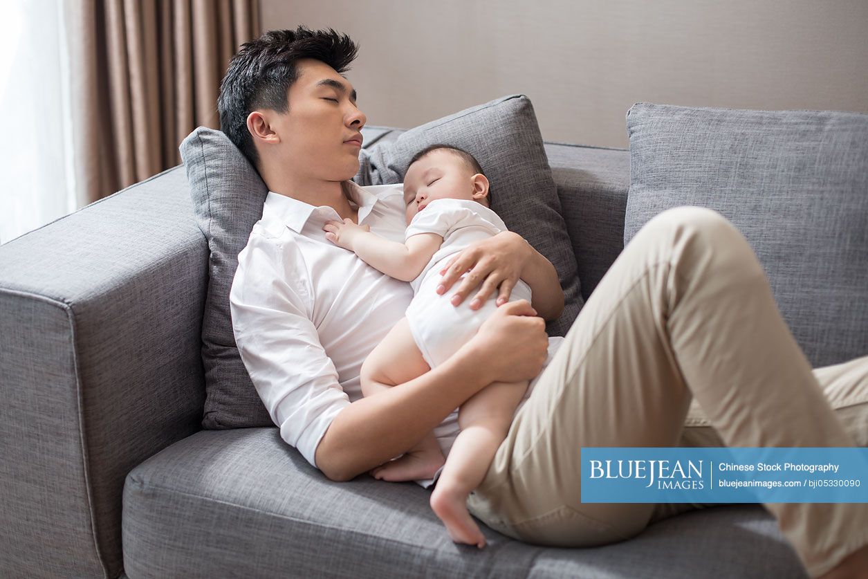 Young Chinese father and baby boy sleeping on sofa