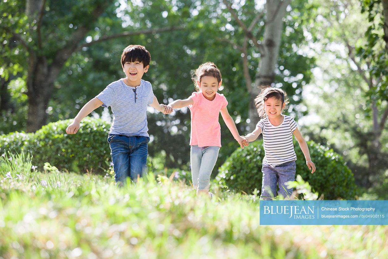 Happy Chinese children holding hands running in woods