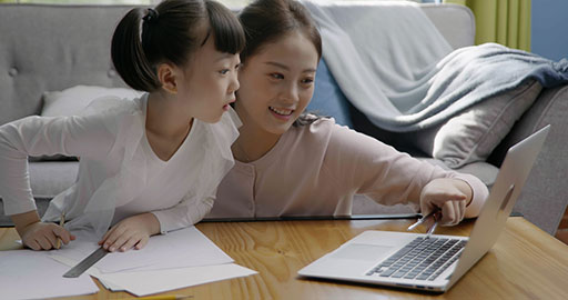 Little girl taking an online class with her mom keeping her company