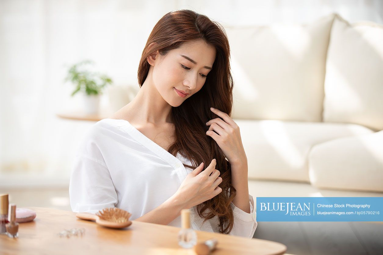 Young Chinese woman with hand in hair at home
