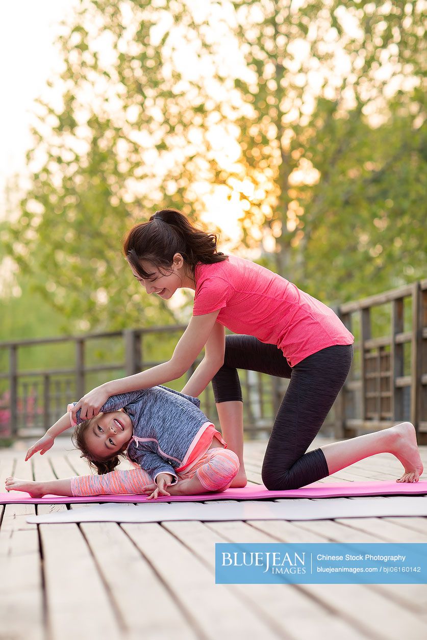 Happy Chinese mother and daughter doing yoga outdoors