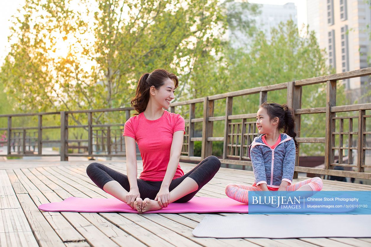 Happy Chinese mother and daughter doing yoga outdoors