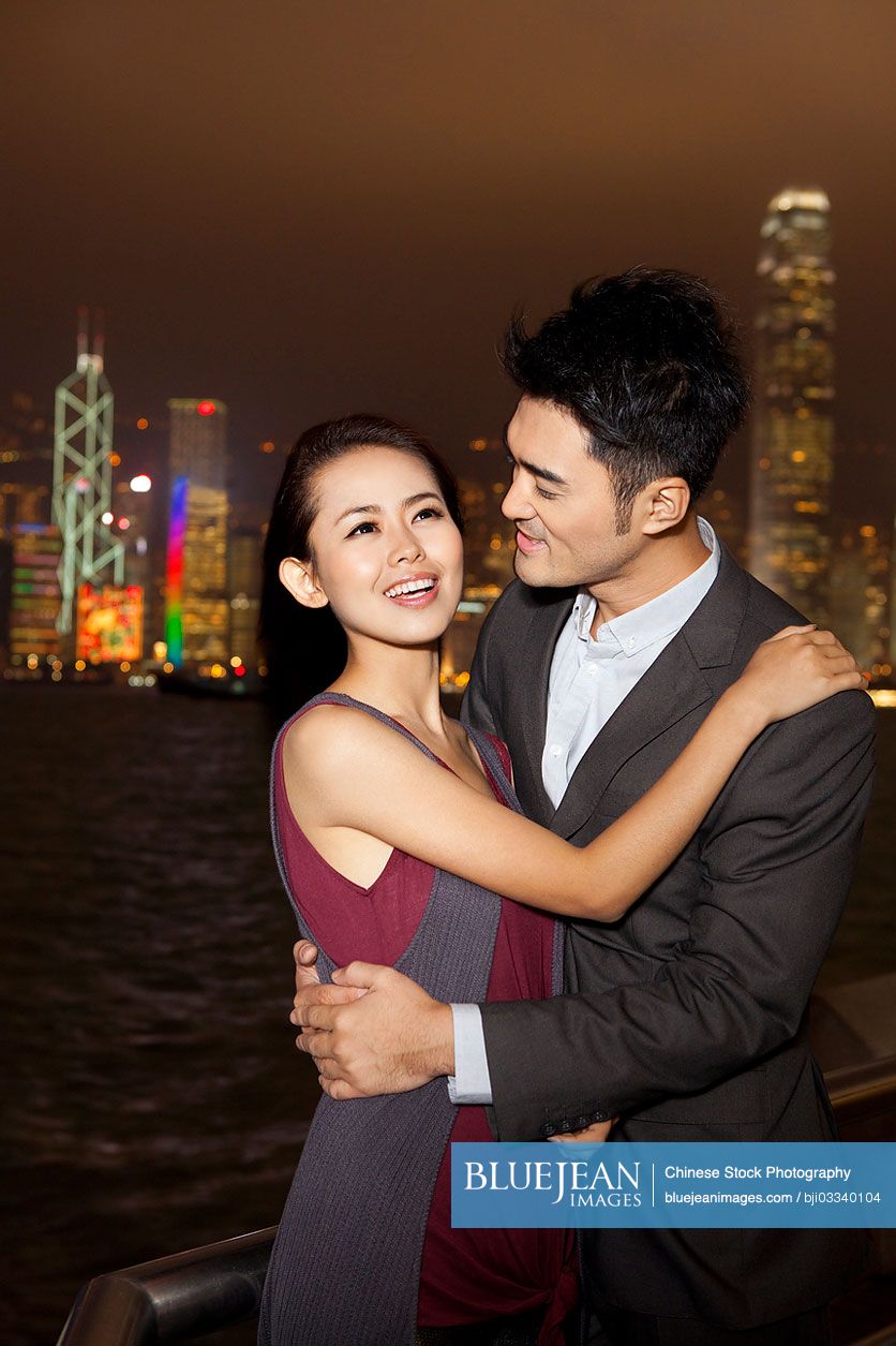 Happy young Chinese couple enjoying the night view of Victoria Harbor ...