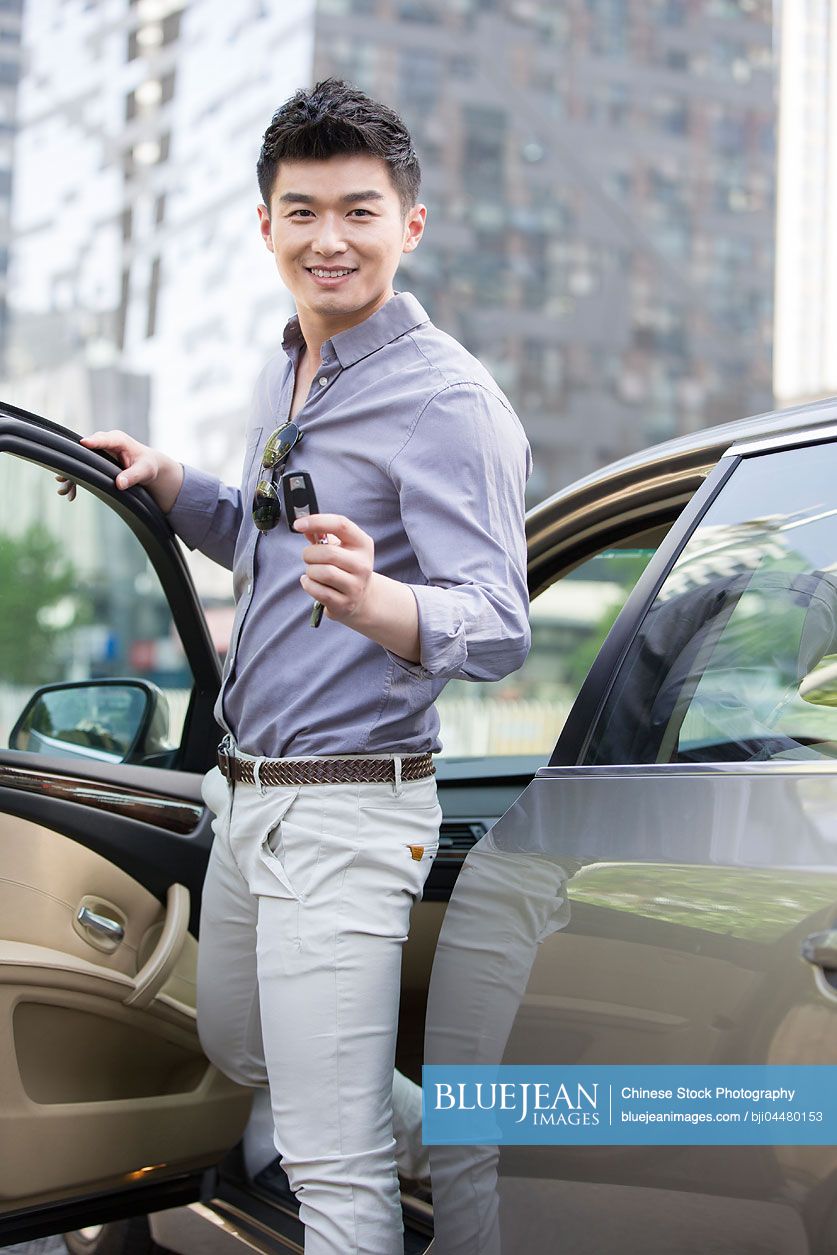 Young Chinese man posing with keys to his new car