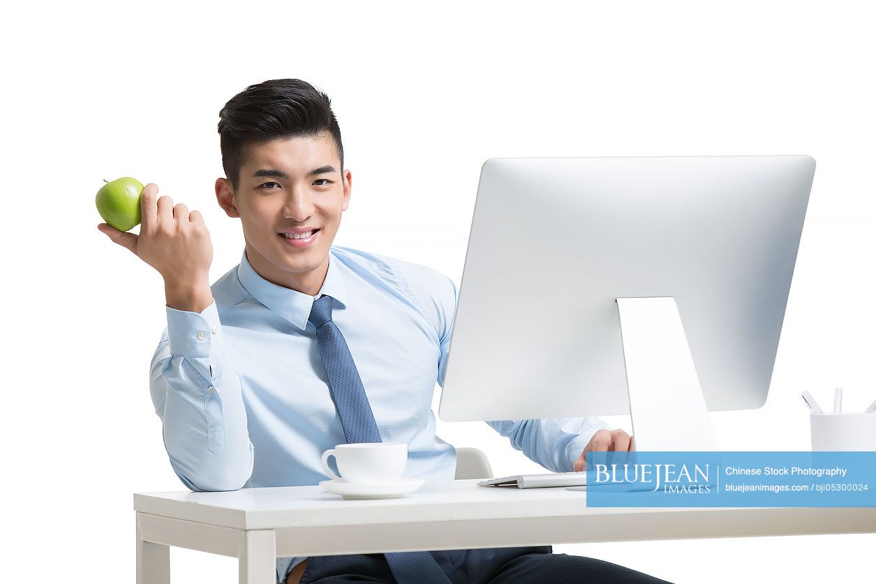 Young Chinese businessman working with computer in office holding apple