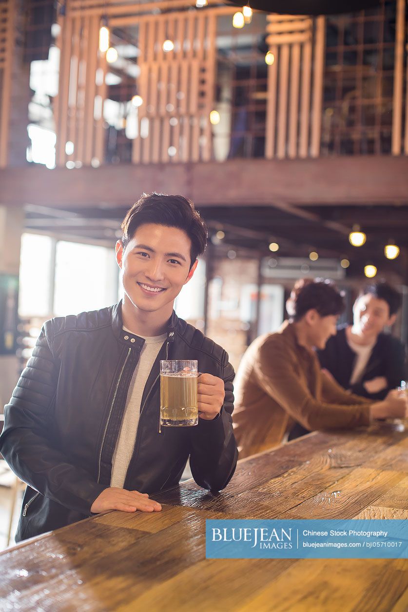 Happy young Chinese man drinking beer in bar