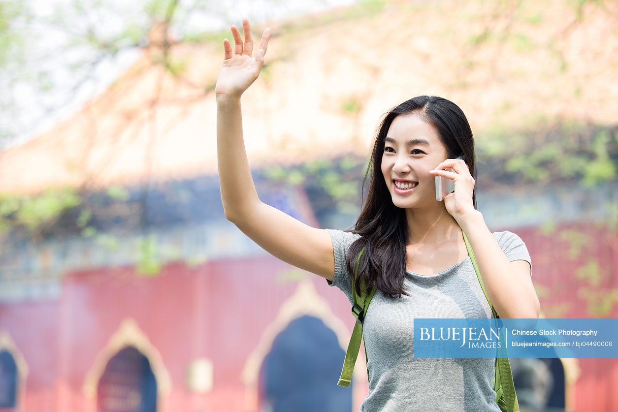 Young Chinese woman talking on the phone and waving