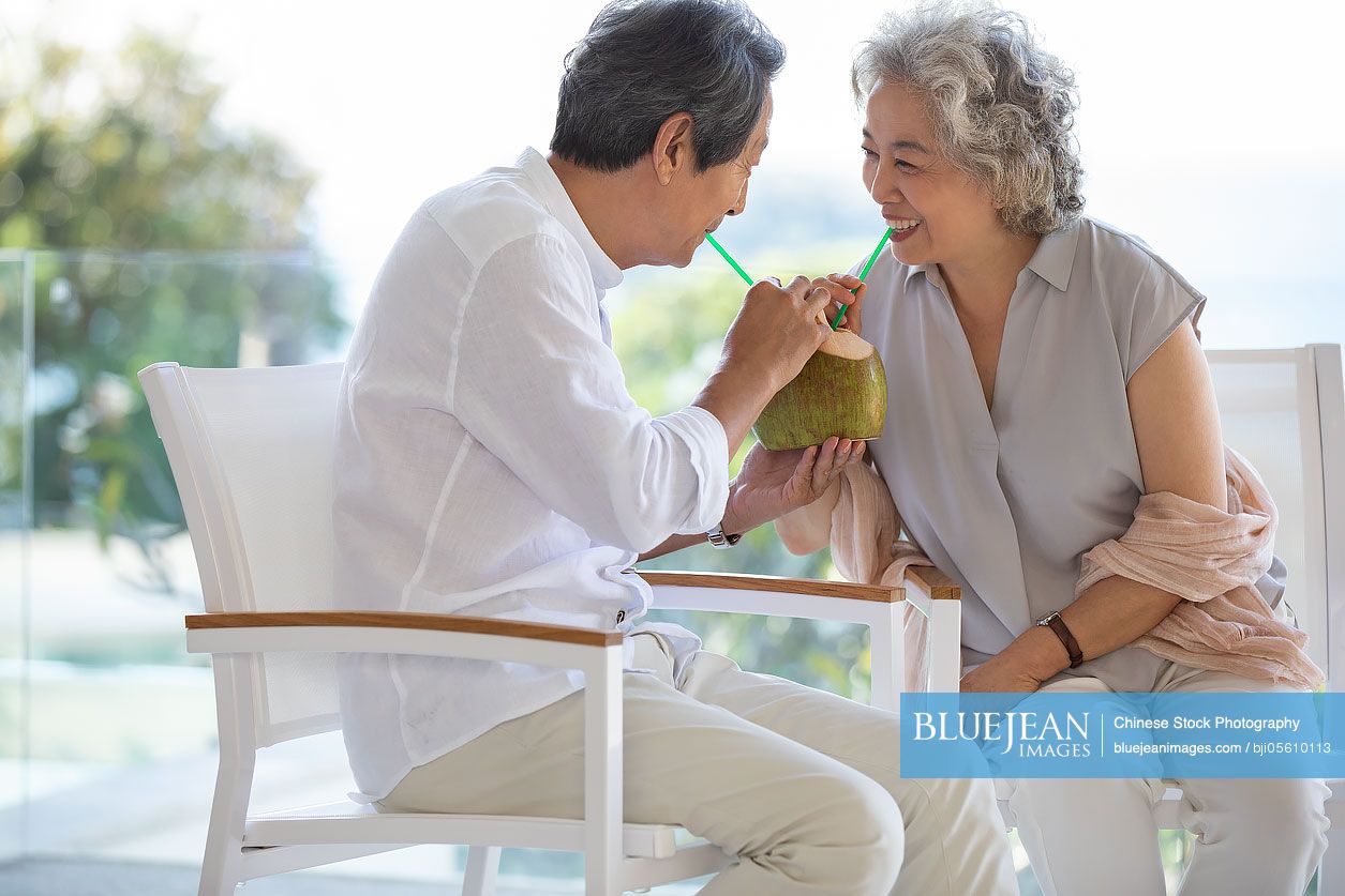 Happy senior Chinese couple drinking coconut milk on balcony