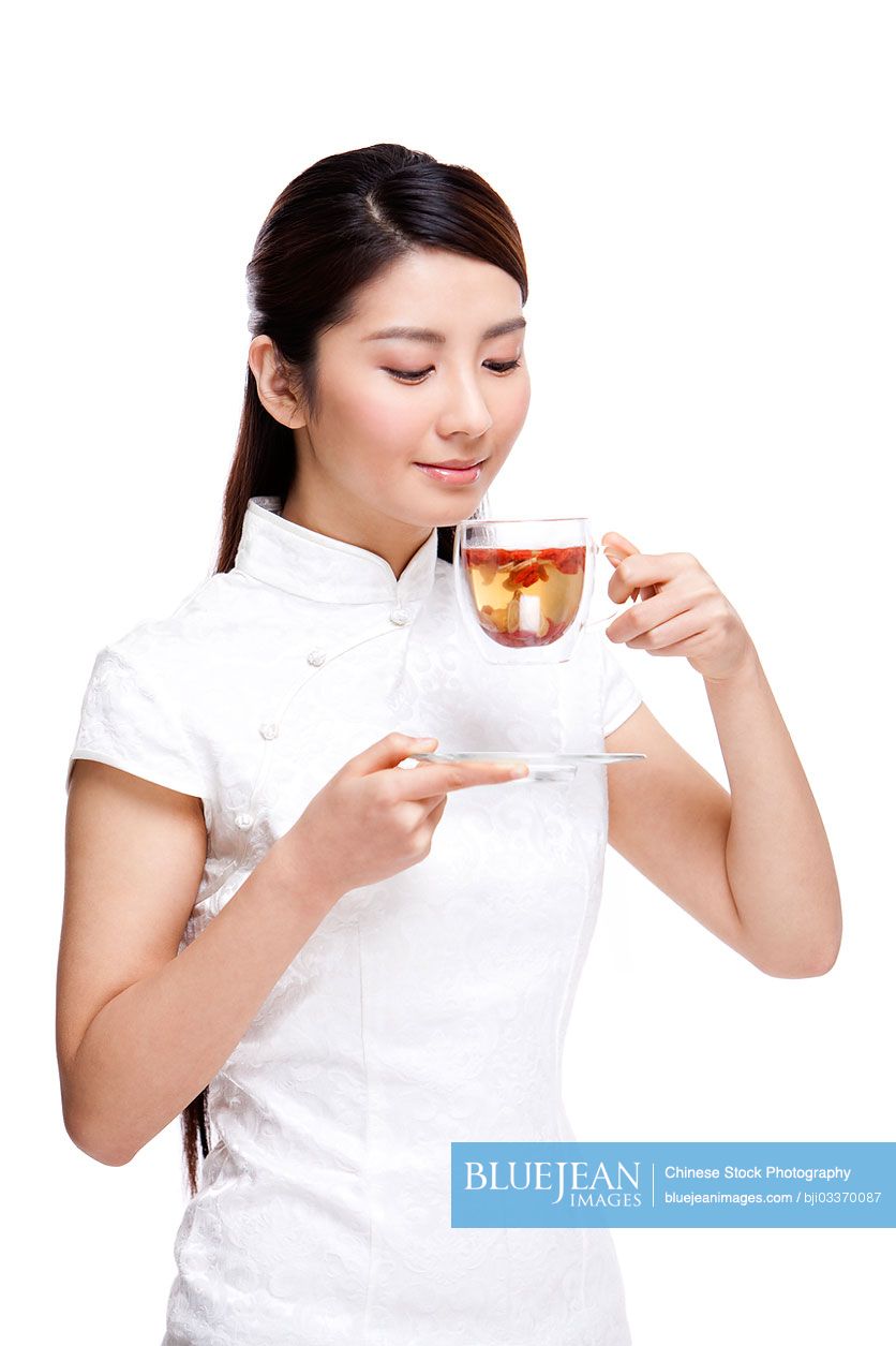 Young beautiful Chinese woman in traditional cheongsam drinking herbal tea