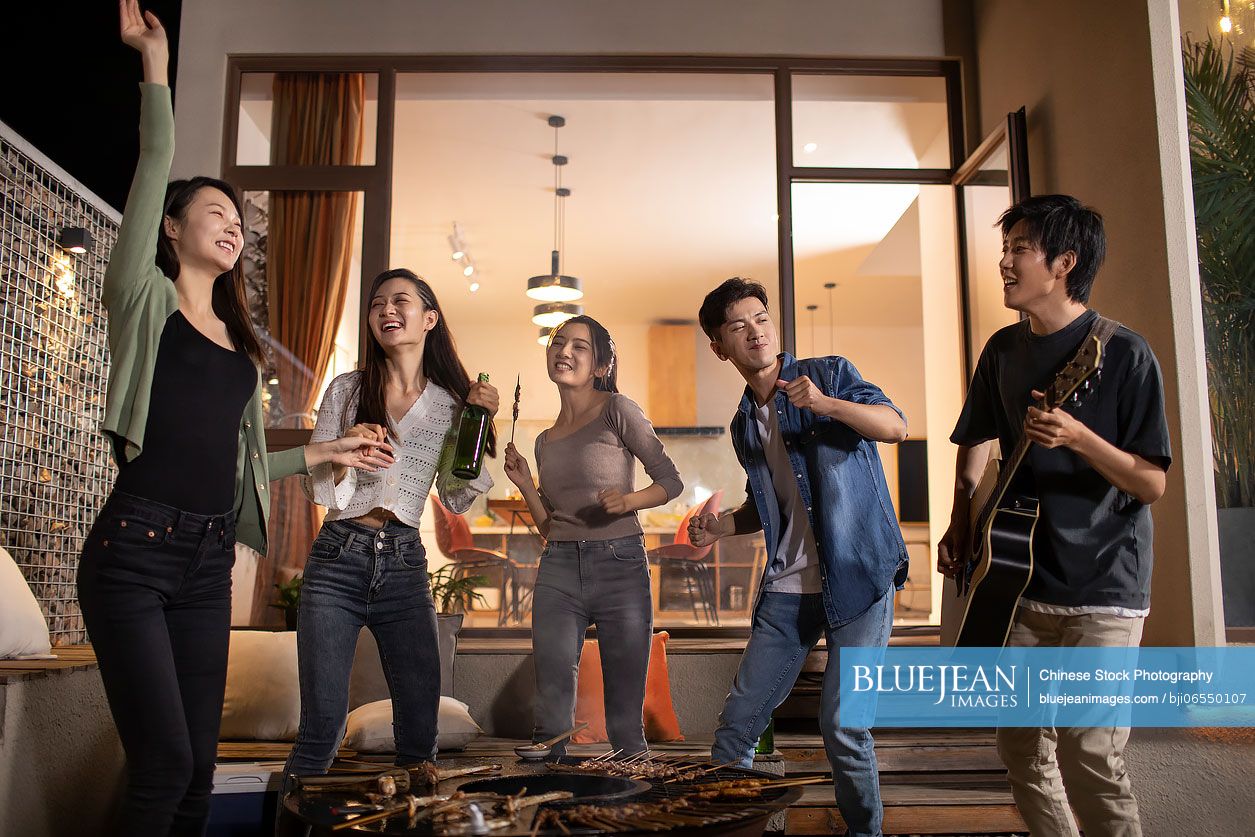 Happy young Chinese friends barbecuing outdoors