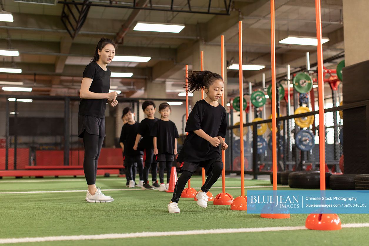 Active Chinese children having exercise class with their coach in gym