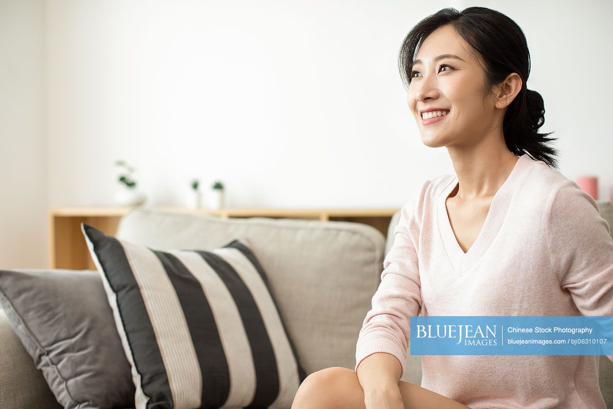 Happy young Chinese woman sitting on sofa