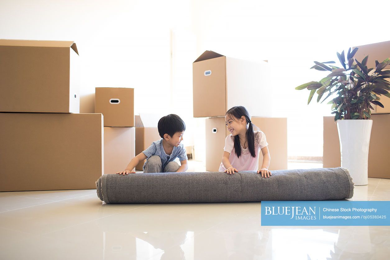 Cute Chinese children unrolling carpet in new house