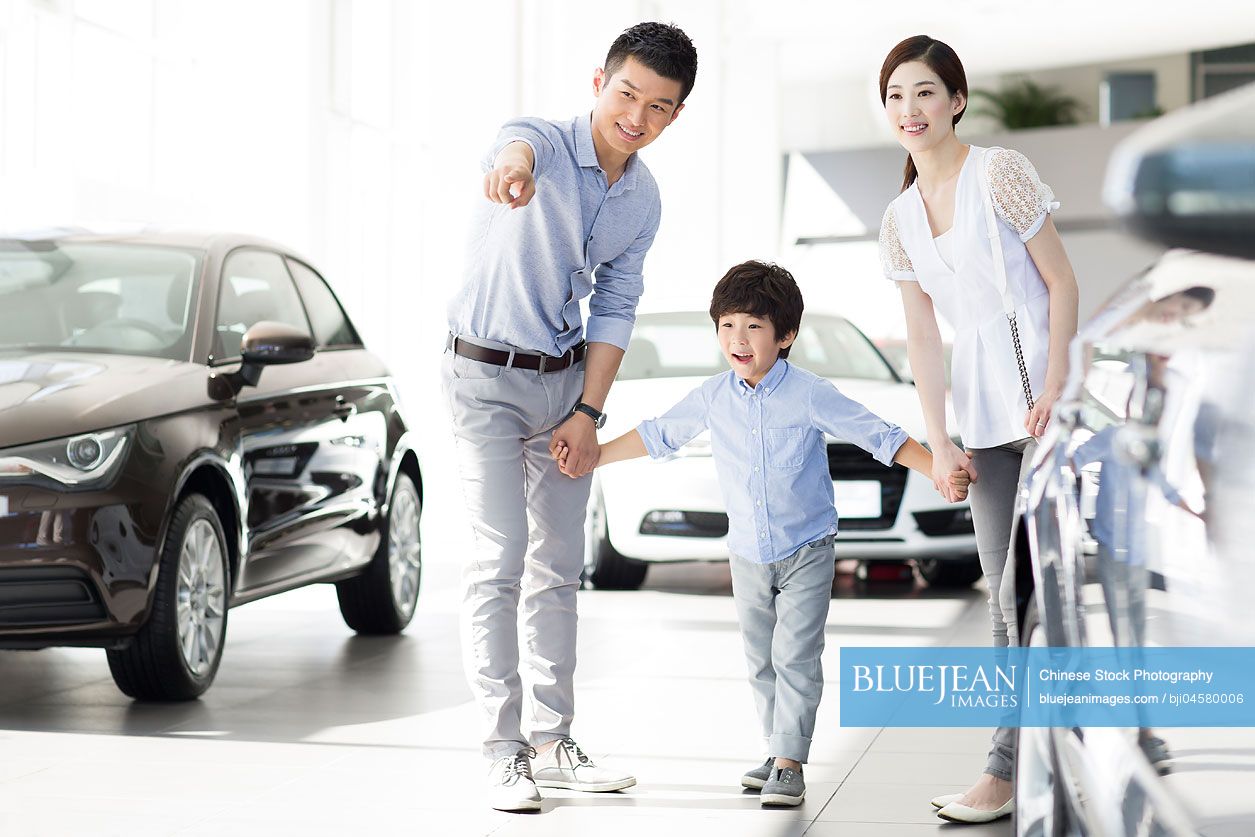 Young Chinese family looking at new car in showroom
