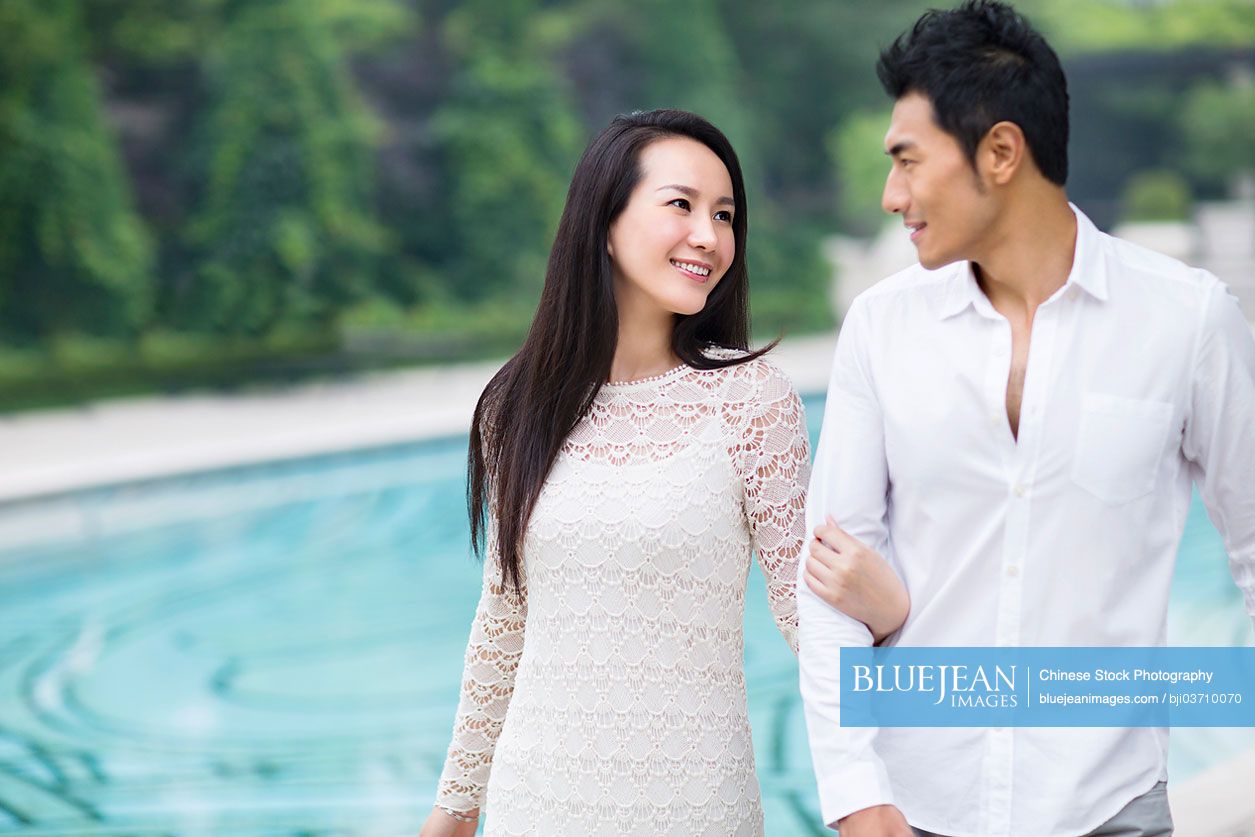 Young Chinese couple walking along poolside