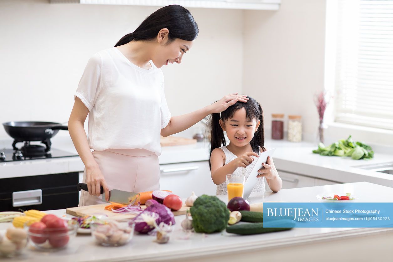 Happy little Chinese girl and mother cooking in kitchen