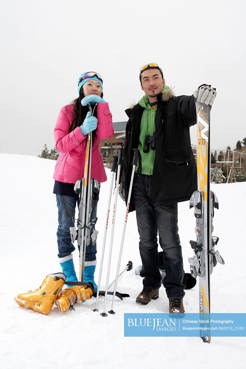 Chinese couple standing on ski field with skis