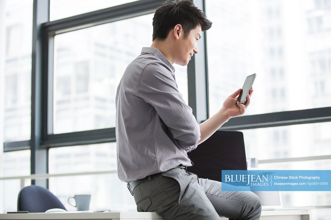 Young Chinese businessman using smart phone in office