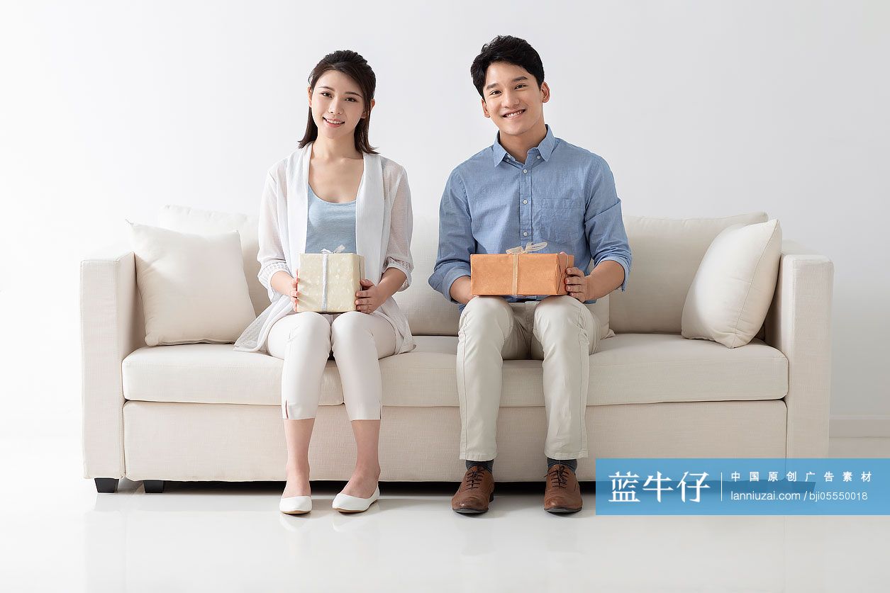 开心的年轻情侣拿着礼物坐在沙发上