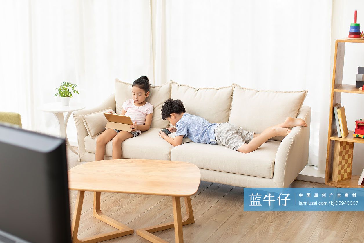 可爱的姐弟俩在沙发上玩电子产品