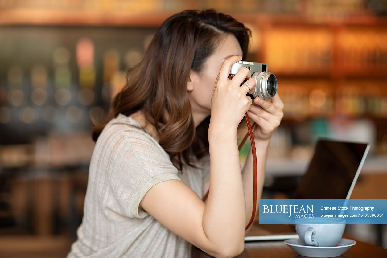 Elegant Chinese woman using digital camera in cafe