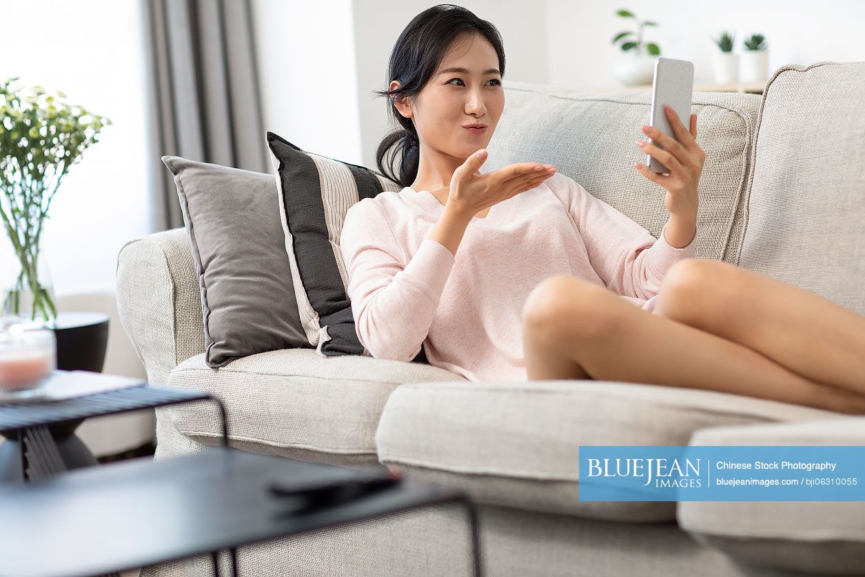Happy young Chinese woman on video call on sofa
