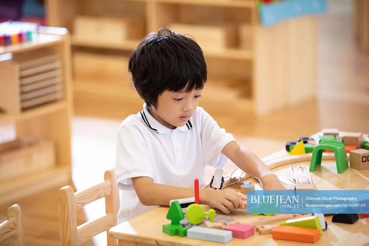 Little Chinese boy playing train set in classroom