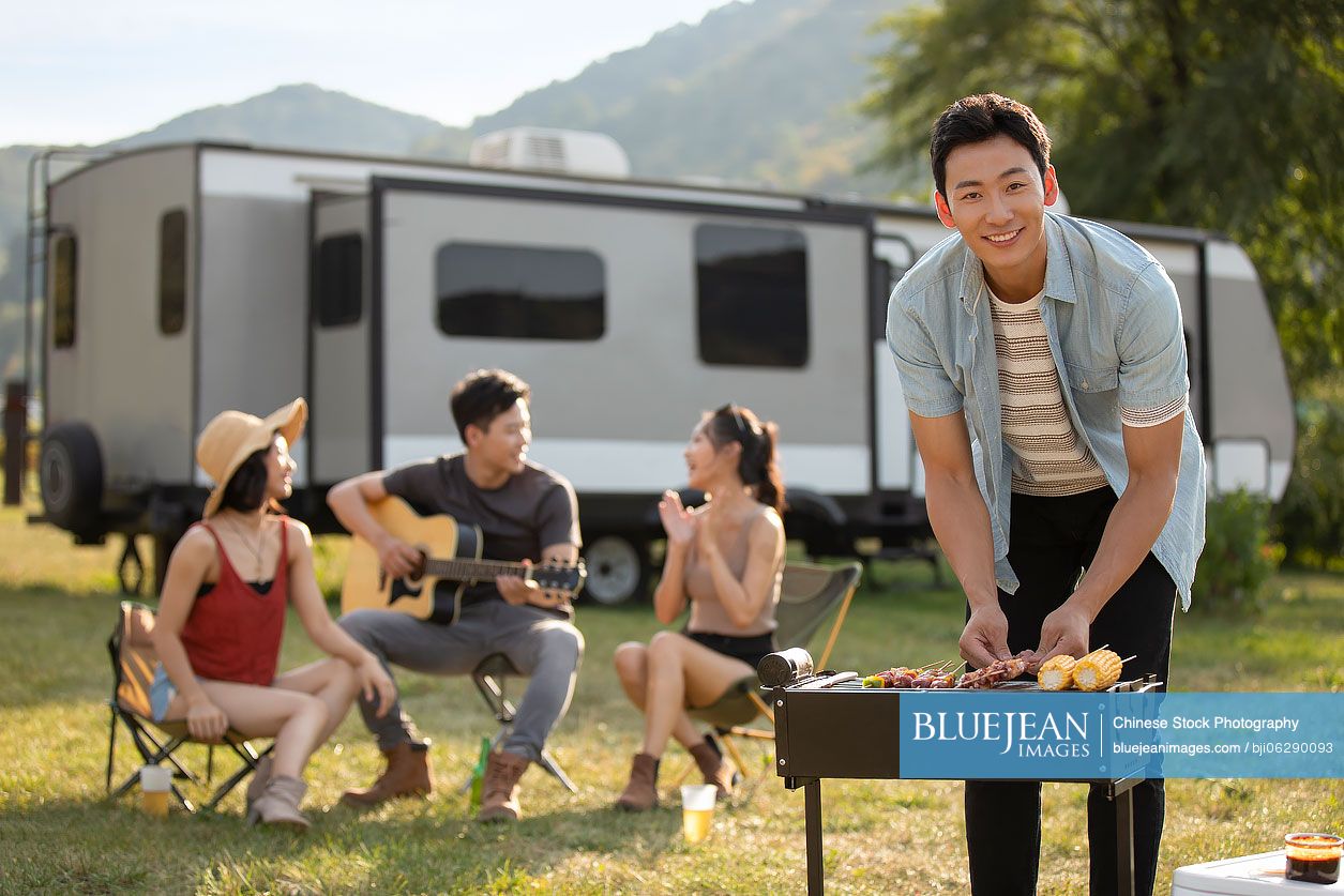 Happy young Chinese friends barbecuing outdoors