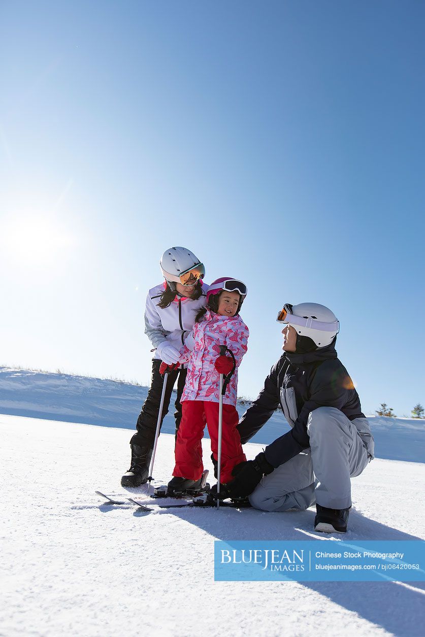 Young Chinese parents teaching daughter to ski