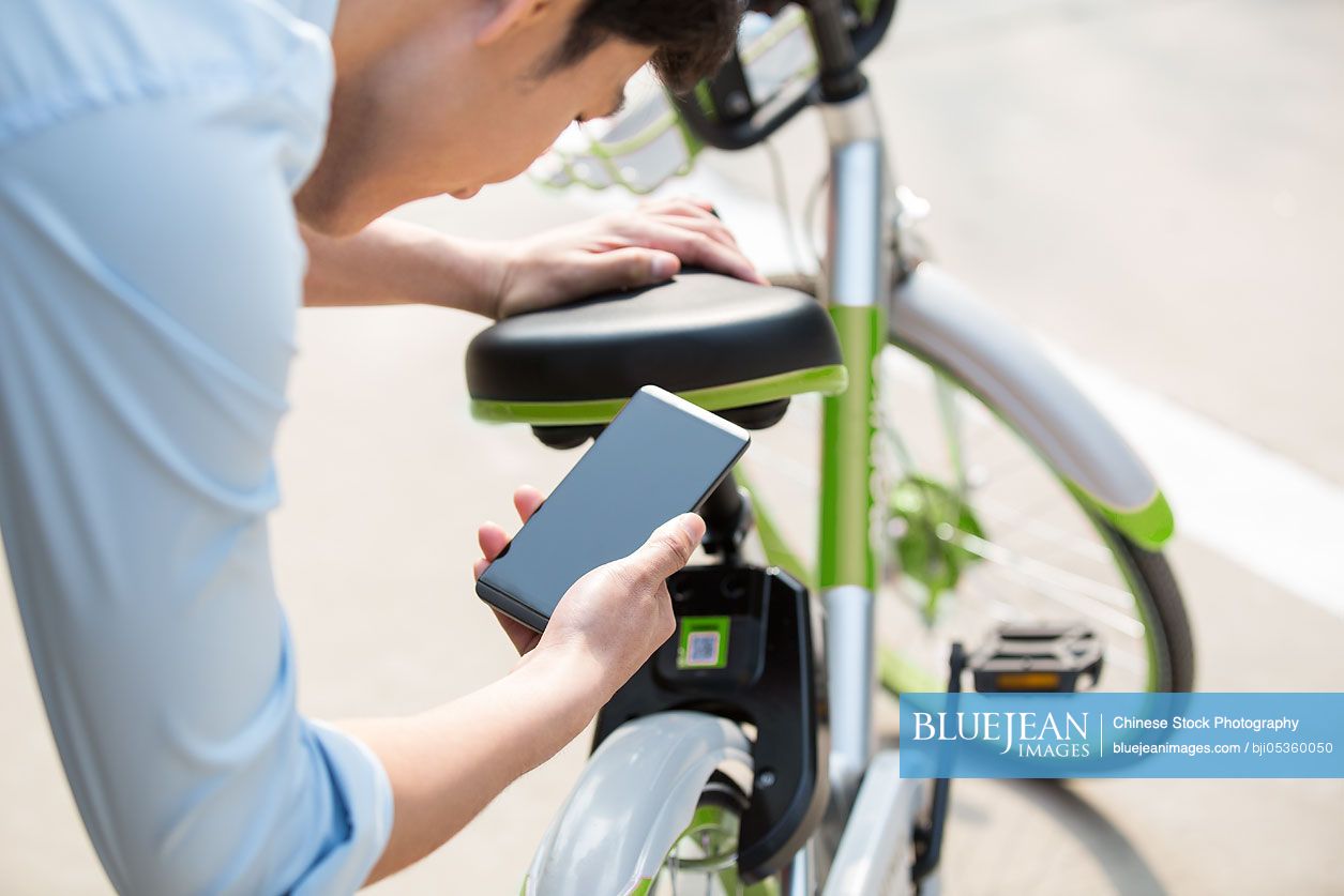 Young Chinese man scanning a QR code to unlock a share bike