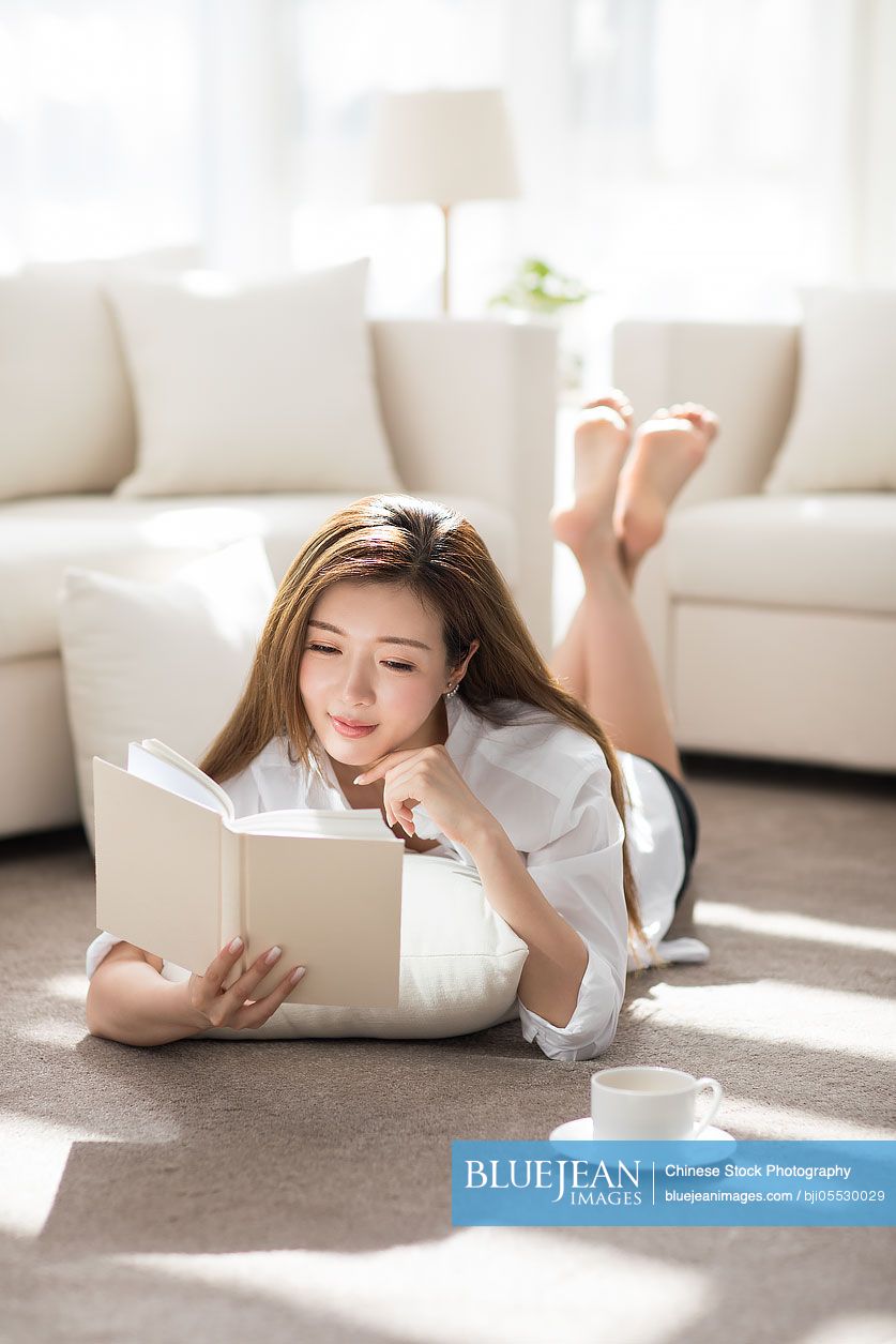 Cheerful young Chinese woman reading a book at home