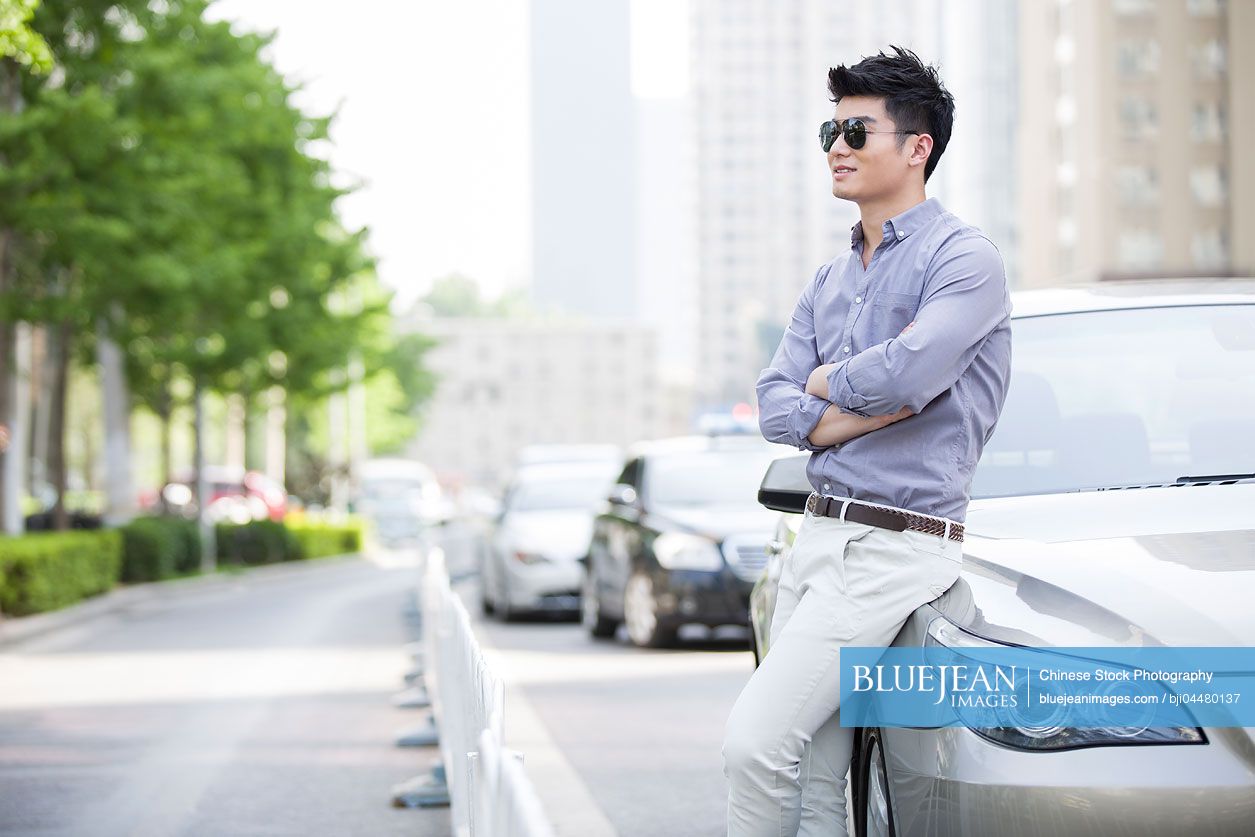 Young Chinese man leaning against his car