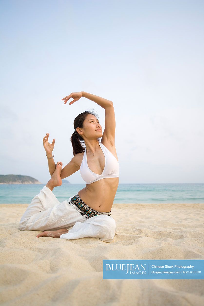 Young Chinese woman doing yoga on the beach