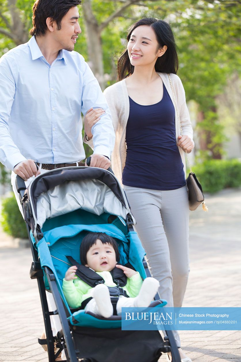 Young Chinese couple taking a walk with their baby in pram