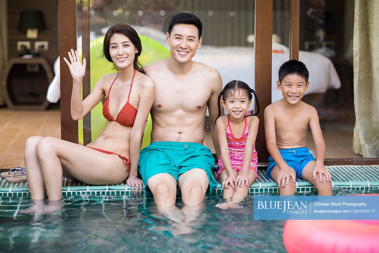 Happy young Chinese family sitting side by side at poolside