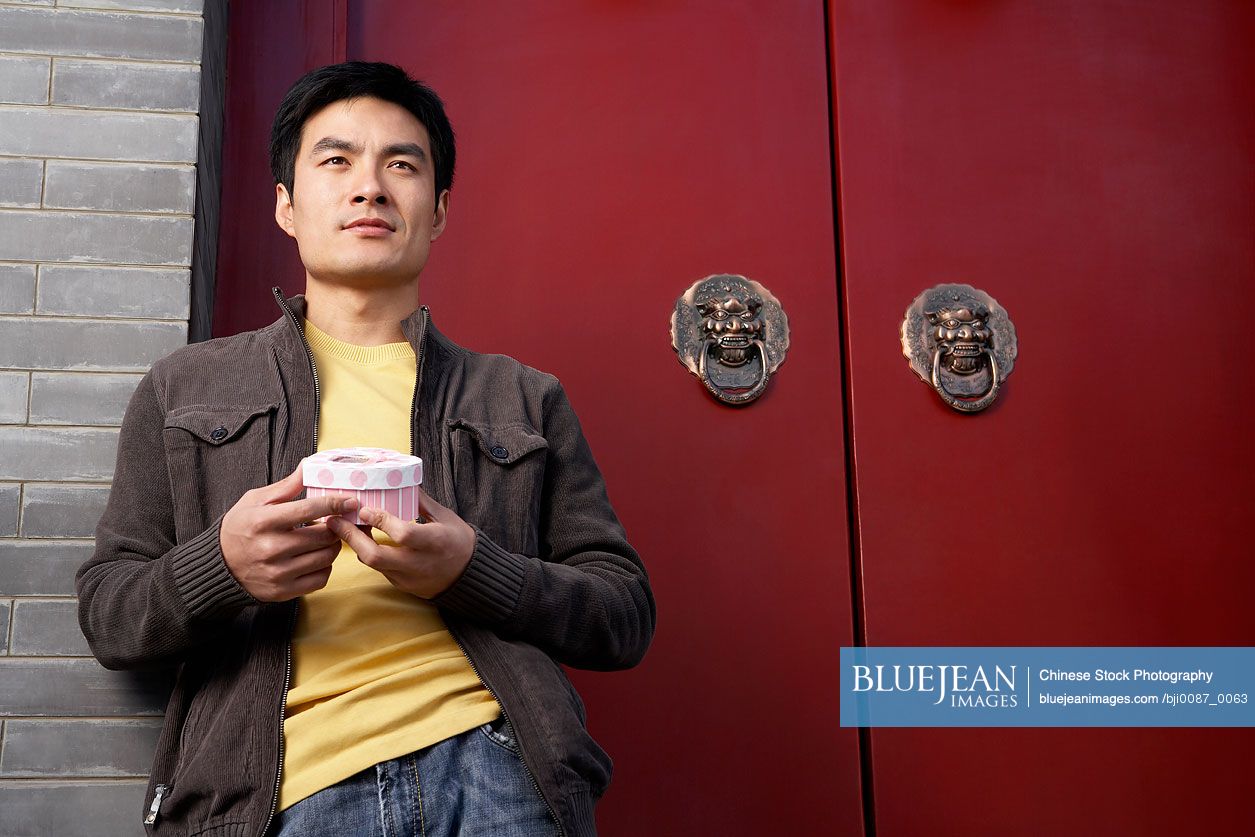 Chinese Young Man Waiting Outside Front Door With A Box Of Chocolates