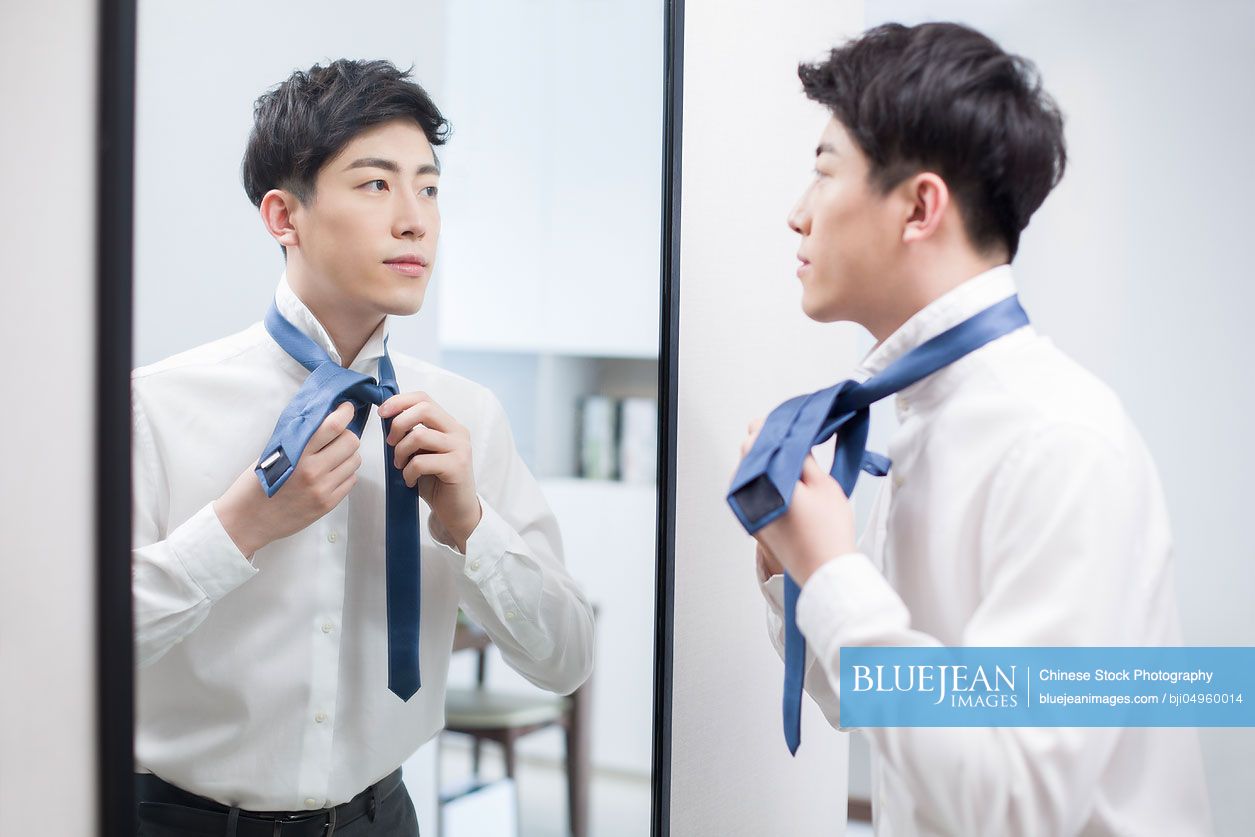 Young Chinese man tying tie in front of mirror