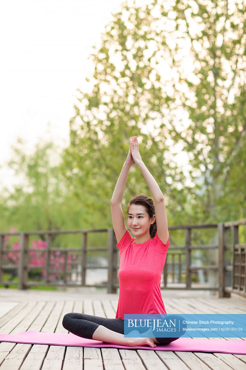 Happy young Chinese woman doing yoga in park