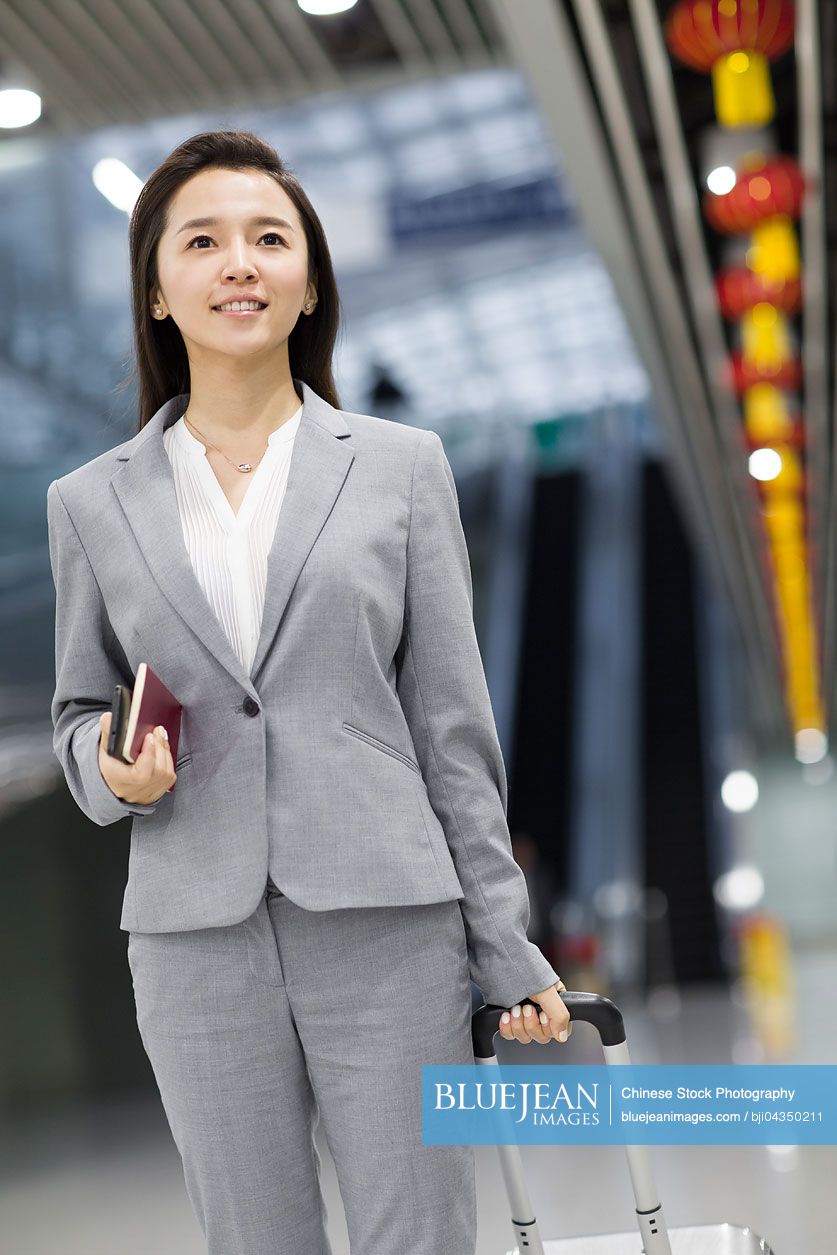 Young Chinese businesswoman walking in airport with suitcase and passport