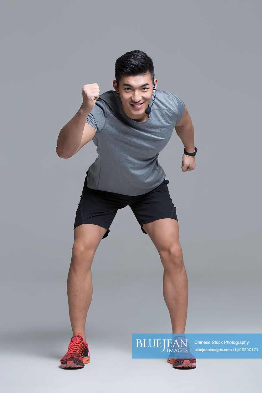 Cheerful young Chinese male trainer with headset teaching at gym