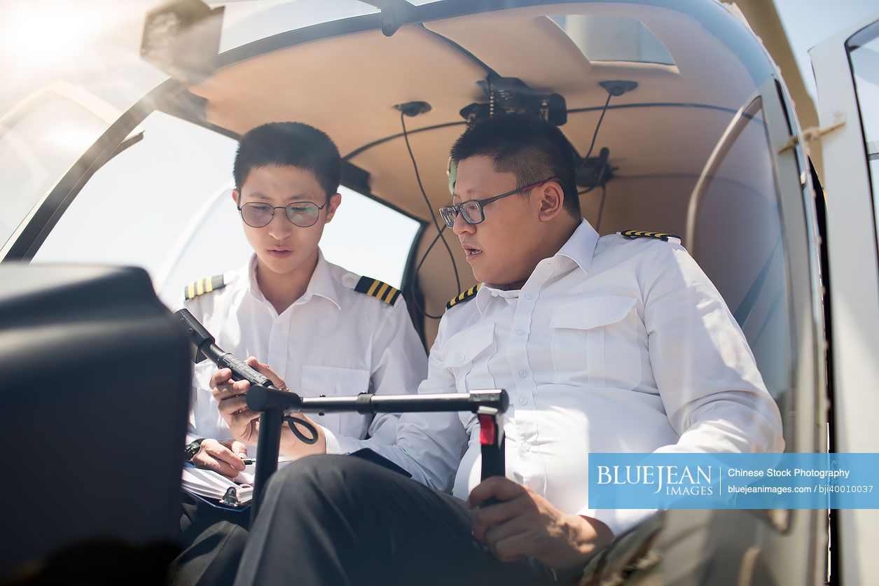 Chinese pilot teaching trainee to operate control panel in cockpit