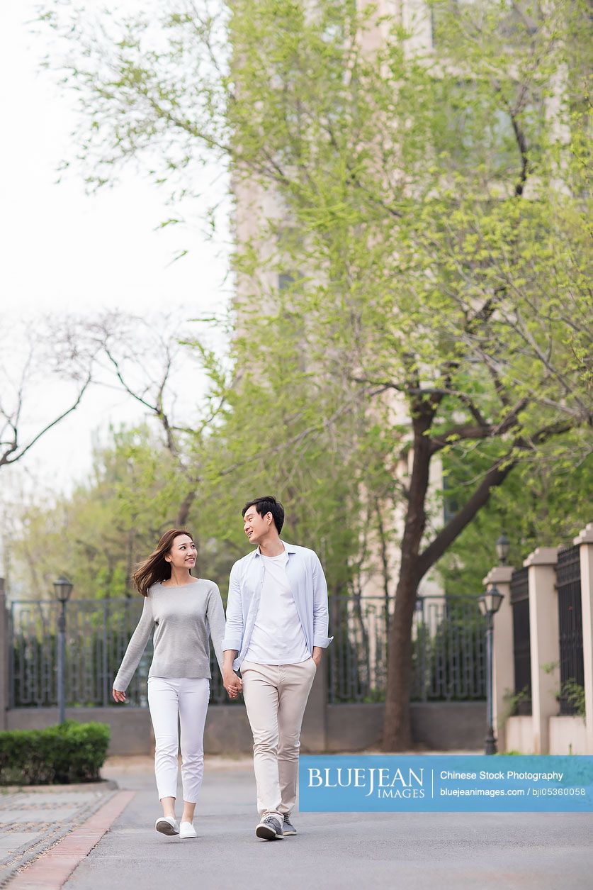 Happy young Chinese couple holding hands walking