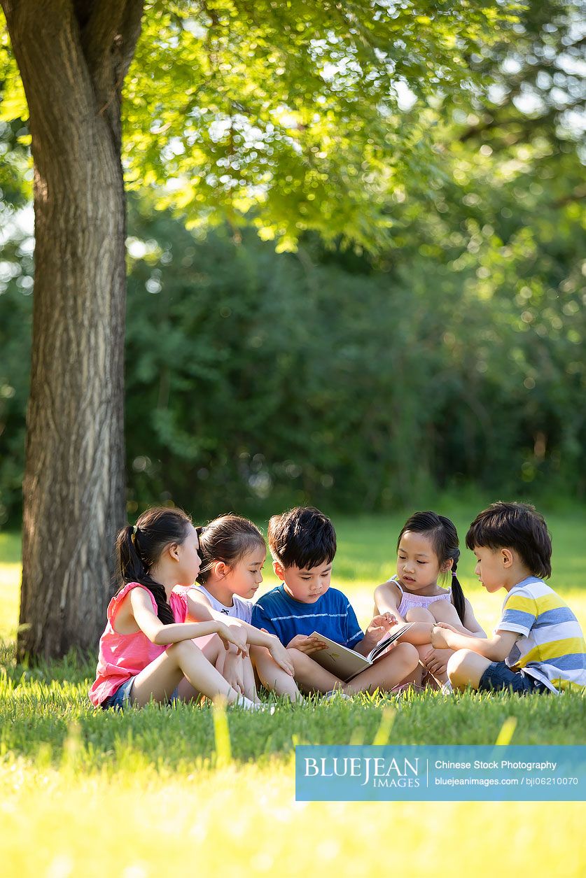 Happy Chinese children reading book on meadow