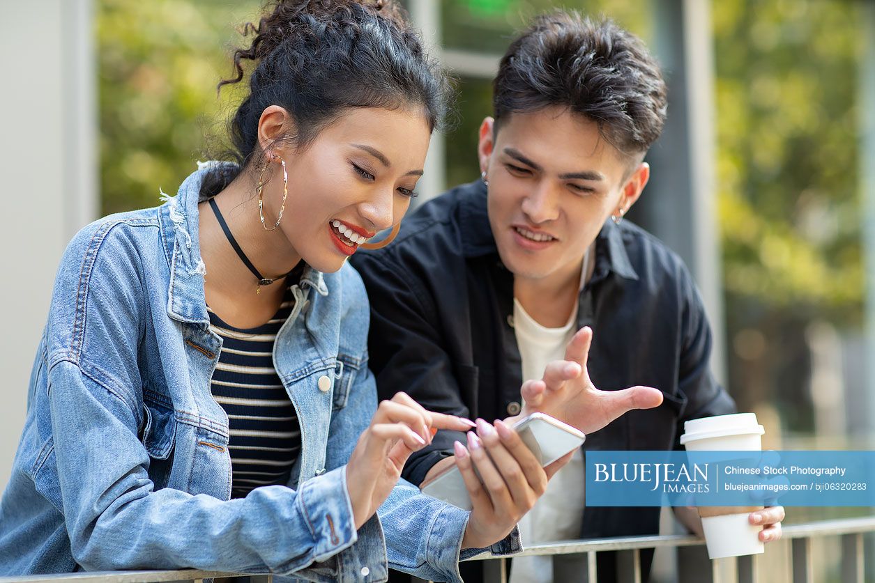 Fashionable young Chinese couple using smartphone on street