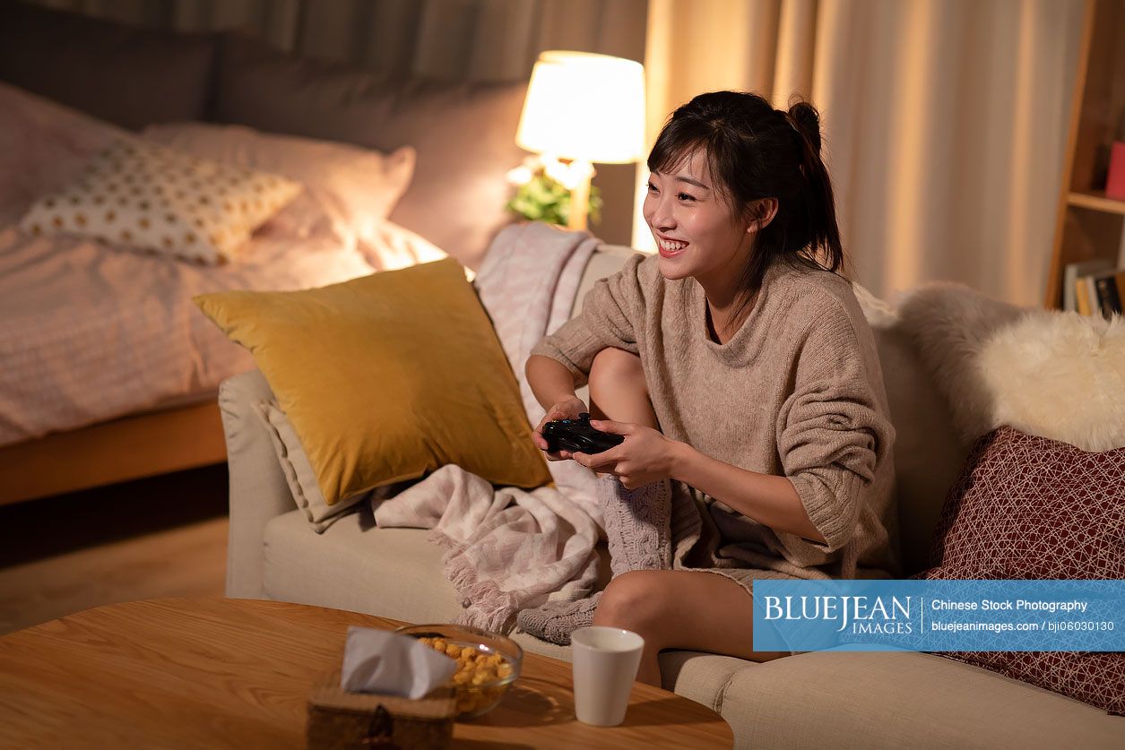Young Chinese woman playing video game on sofa